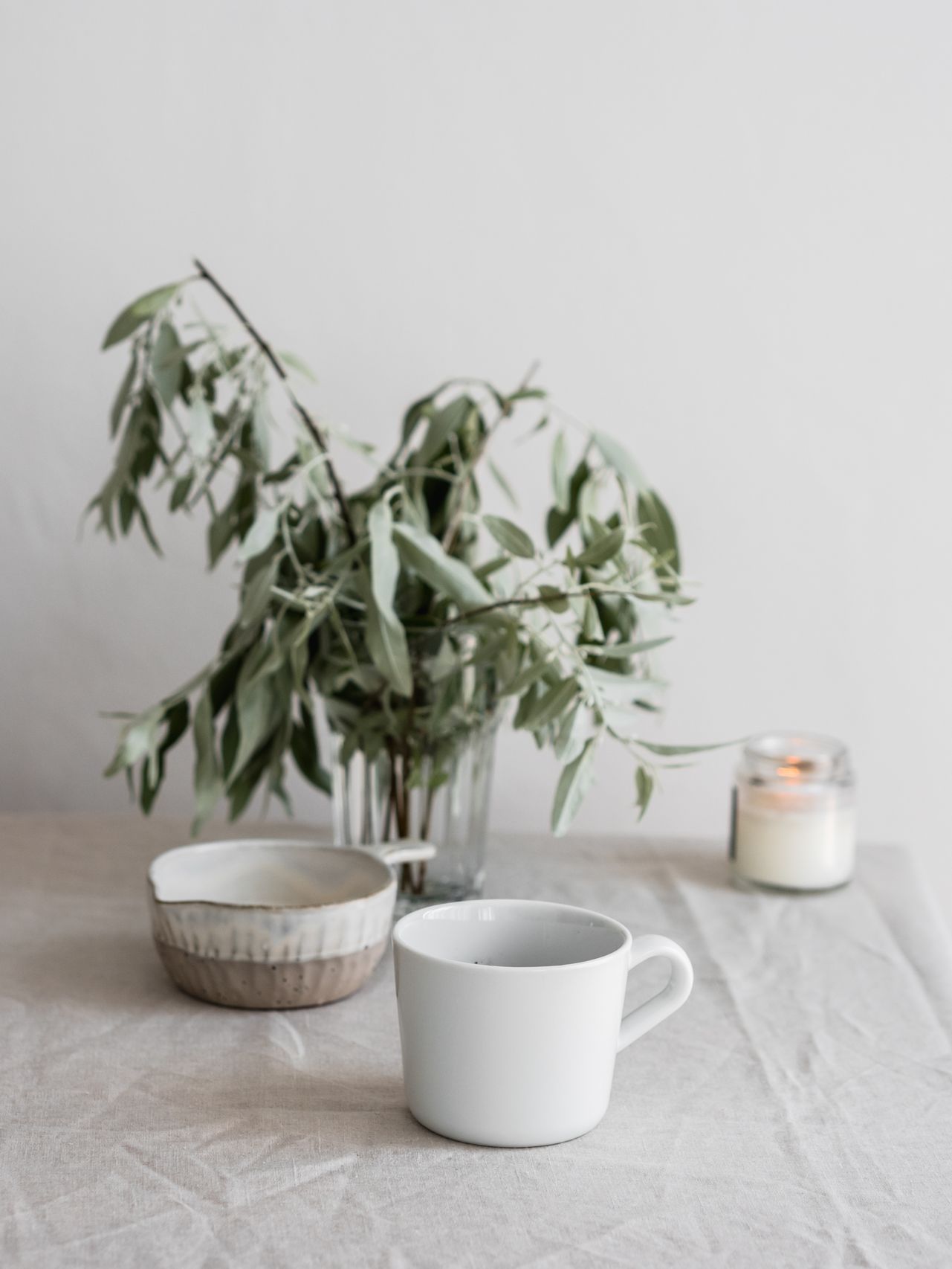 Ceramic vase with eucalyptus branches, lit candle in a small dish, and a brass singing bowl with a mallet